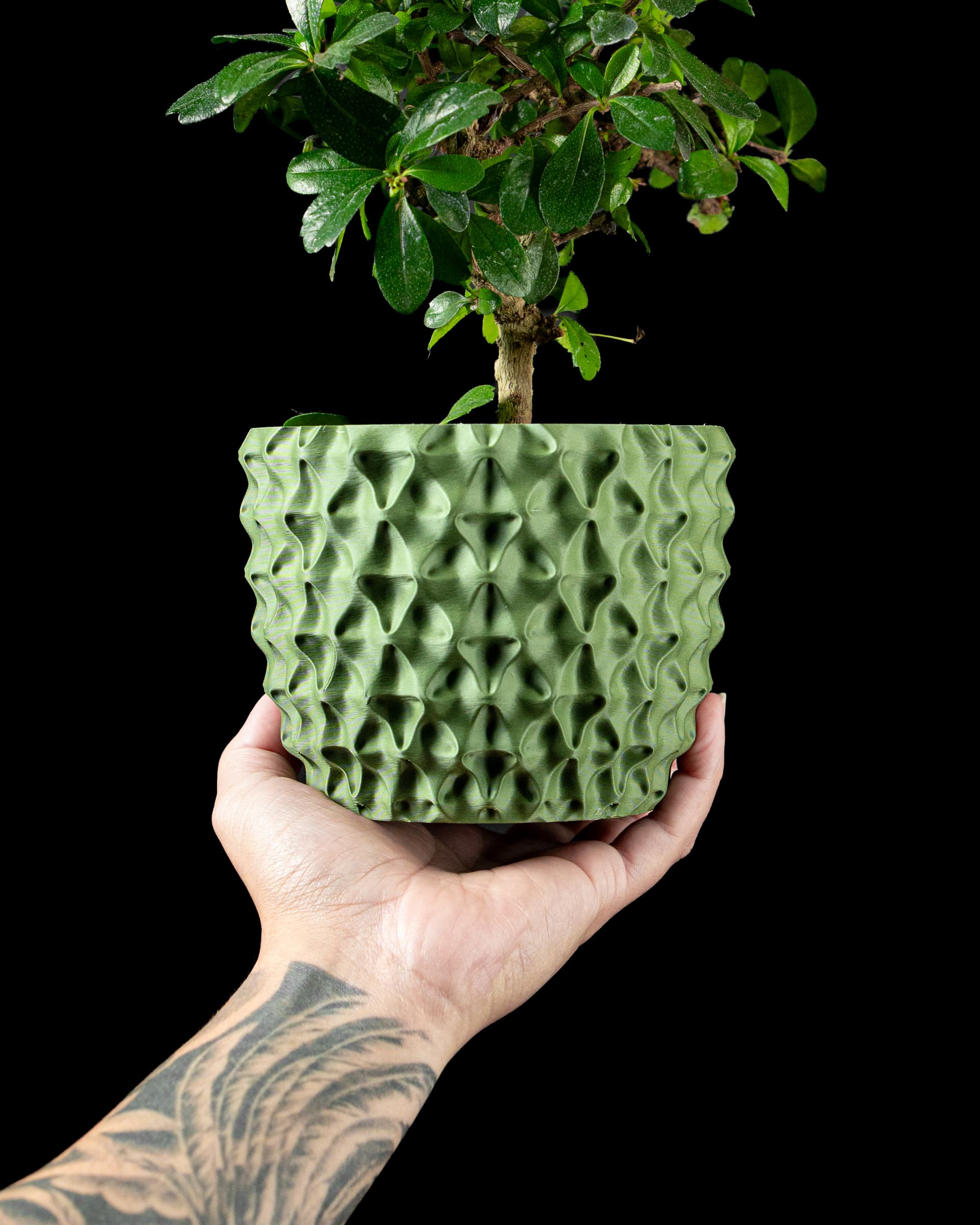 3D-Blumentopf Tri-Wave Planter — dreieckige Wellenmulden in Olivgrün, bauchige Form, Hand hält Topf