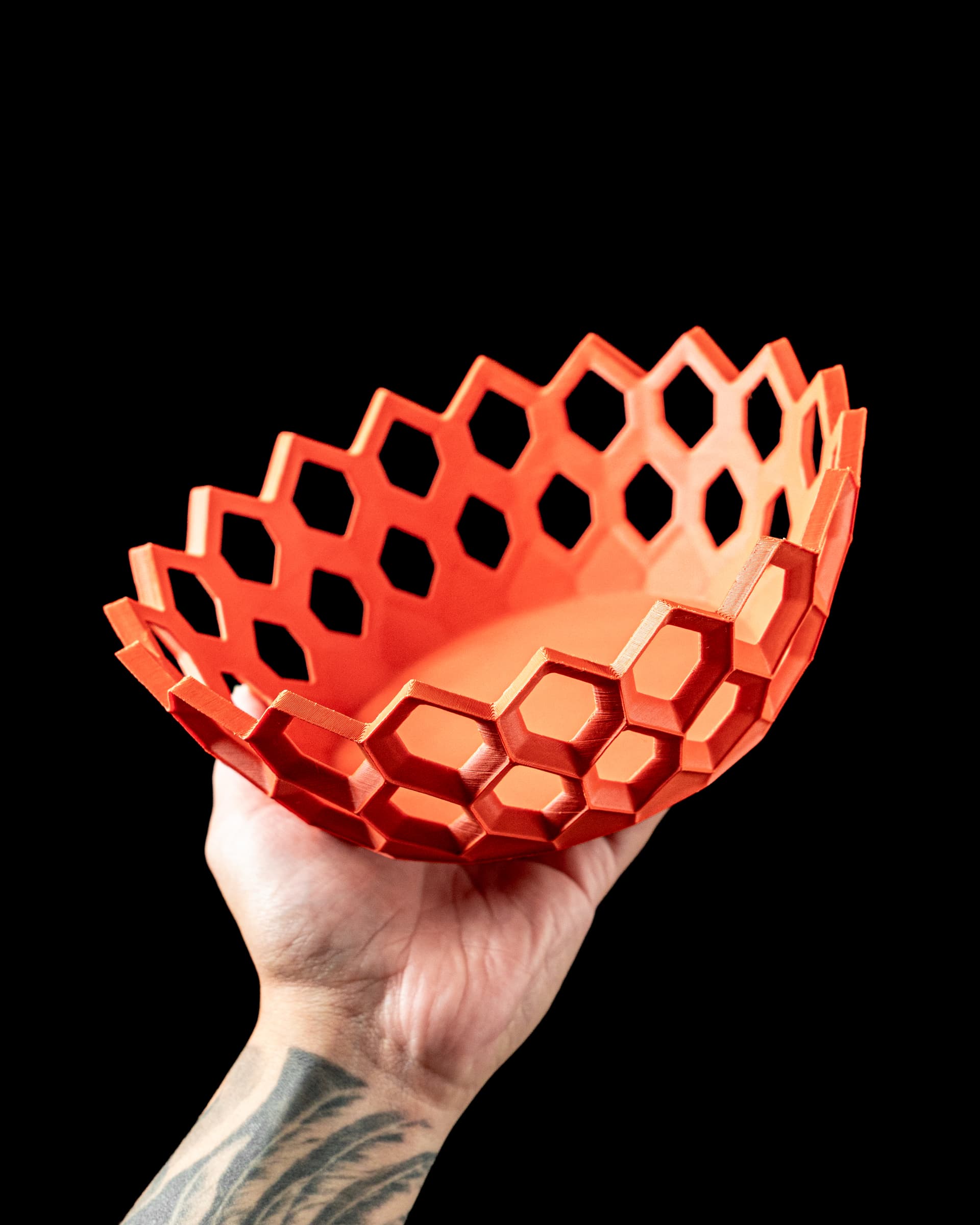 Hexa Catch-all Bowl 3D-Druck in Orange-Rot — Schale mit offenem Sechseck-Gittermuster, in tätowierter Hand vor schwarzem Hintergrund