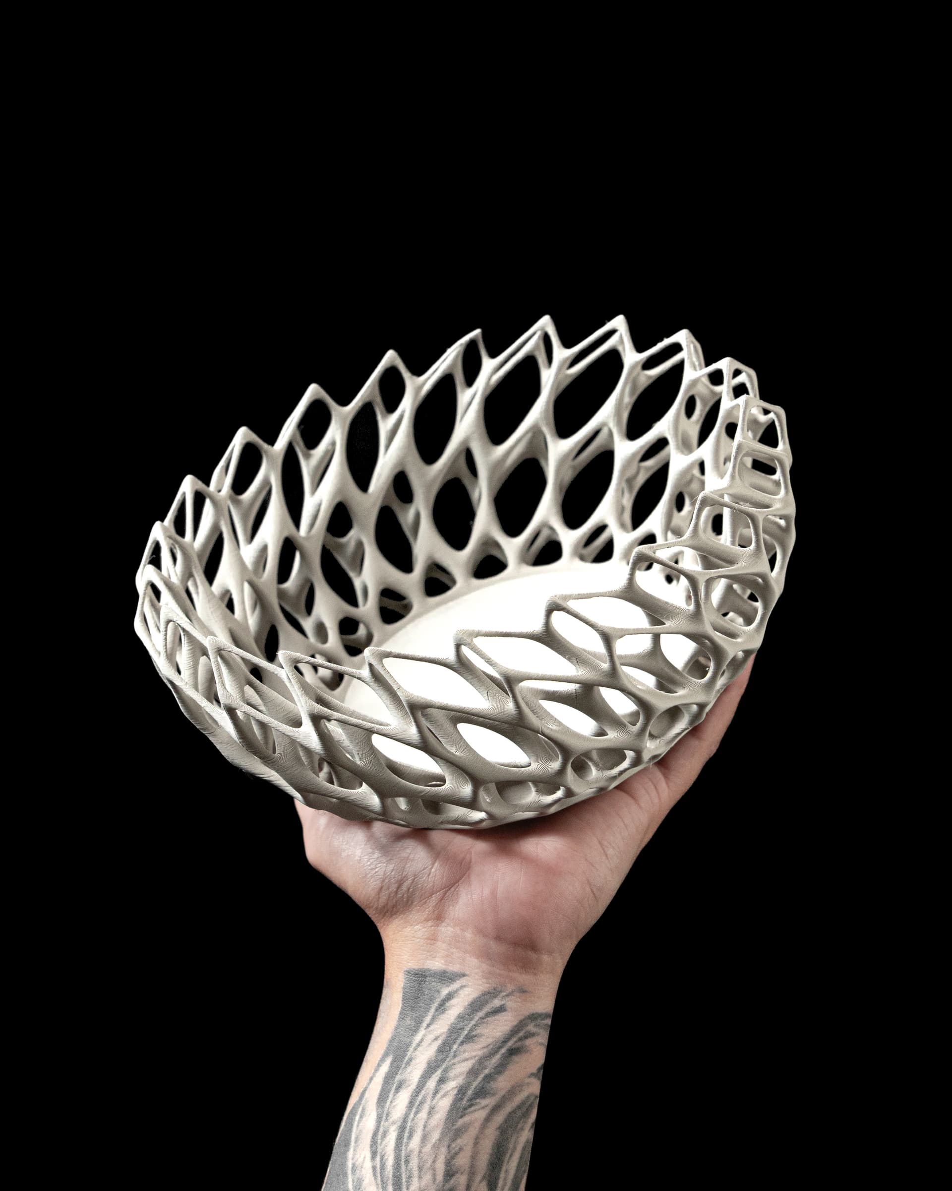 Twisted Catch-all Bowl 3D-Druck weiß — organisches Gitternetz mit geflochtener Twisted-Struktur, in tätowierter Hand vor schwarzem Hintergrund