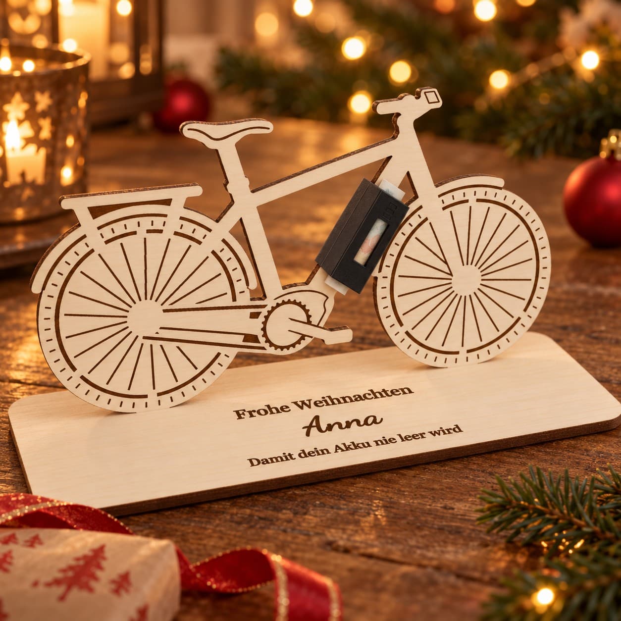 E-Bike aus Pappelholz mit Lasergravur auf personalisierter Grundplatte „Frohe Weihnachten · Anna · Damit dein Akku nie leer wird“, im schwarzen Akku steckt ein gerollter Geldschein (Produktvisualisierung)