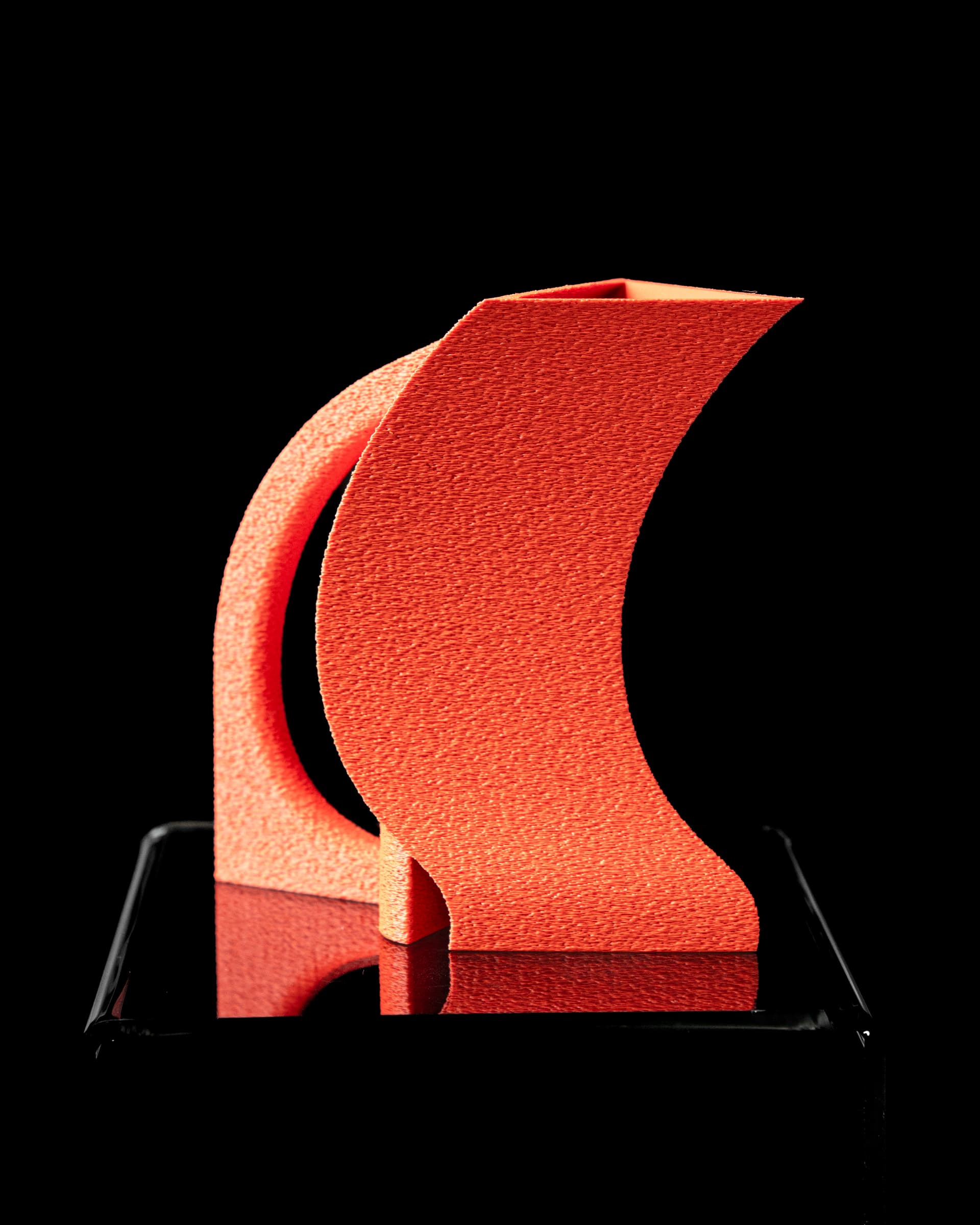 Vorto Watering Can 3D-Druck orange-rot — skulpturale mondsichelförmige Gießkanne mit strukturierter Oberfläche und eckigem Ausguss, auf Podest
