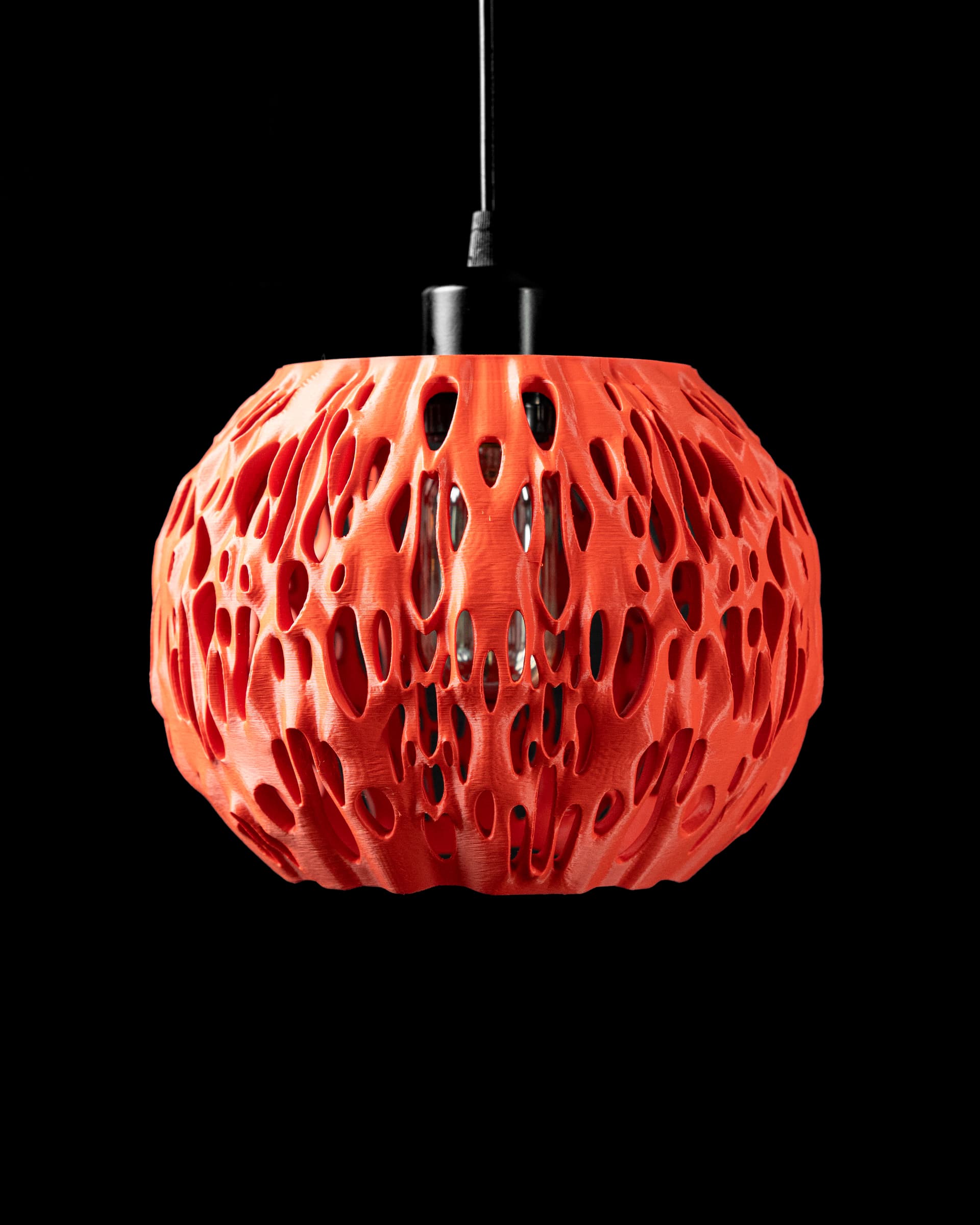 3D-Pendelleuchte Spotted — Kugelform Orange-Rot, organische durchbrochene Poren-Textur, beleuchtet