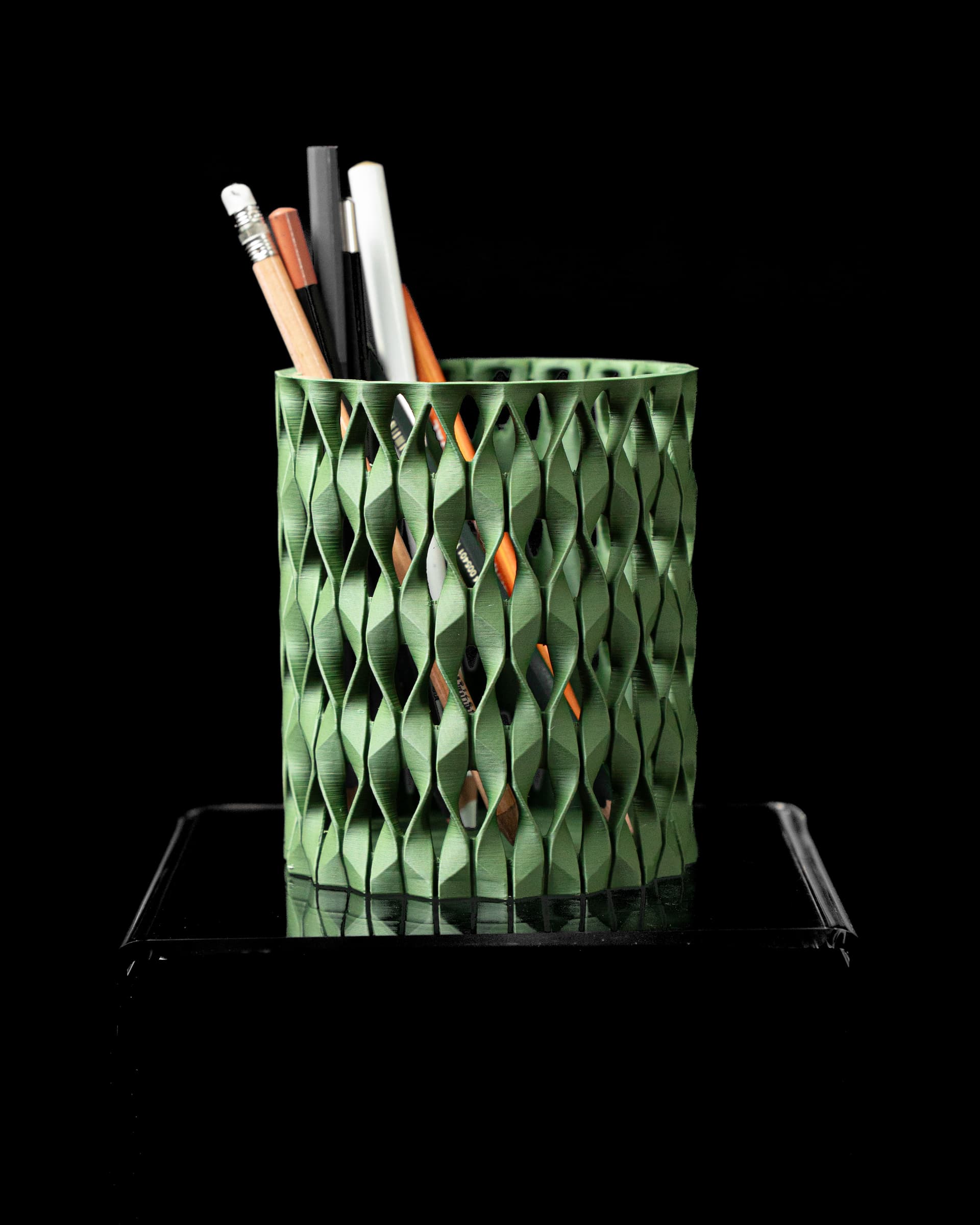 Chain Pencil Holder 3D-Druck grün — zylindrischer Stiftehalter mit Kettenglied-Flechtmuster, mit Stiften befüllt auf Podest
