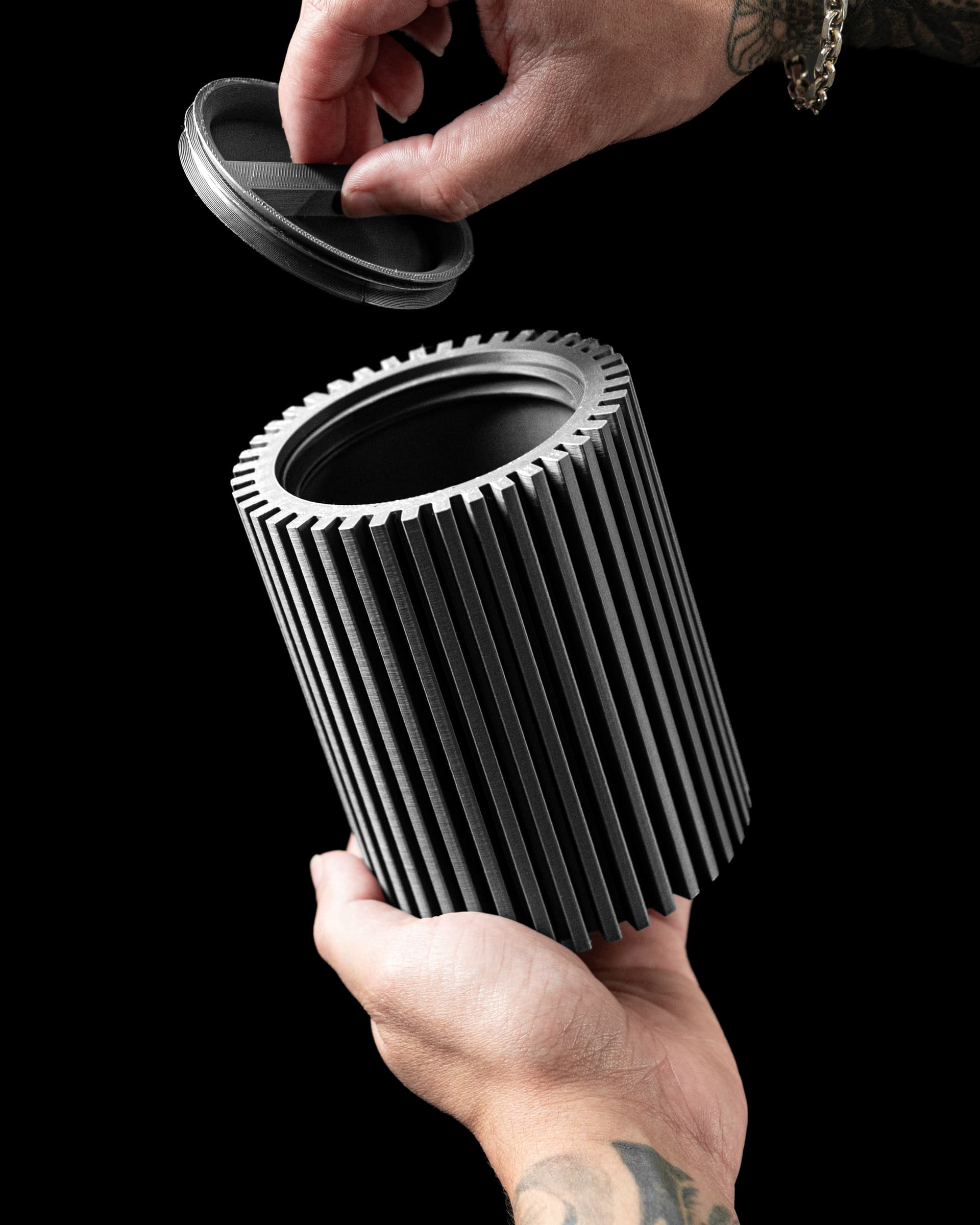 Striped Storage Container 3D-Druck dunkelgrau — zylindrische Dose mit Vertikalrippen und Zahnrad-Deckelrand, geöffnet von zwei Händen