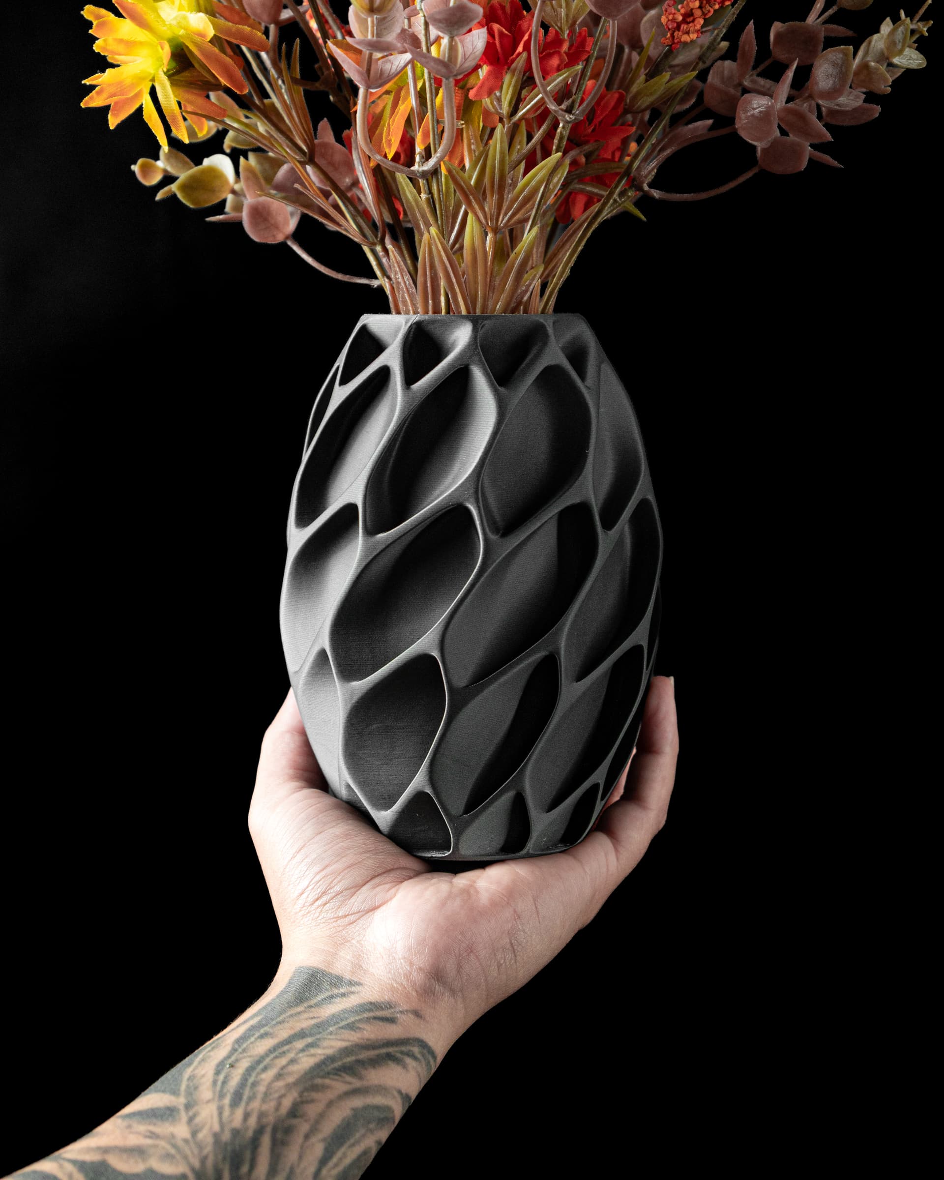 Exo Flower Vase schwarz — ovale Waben-Netzstruktur, in tätowierter Hand mit buntem Herbststrauß