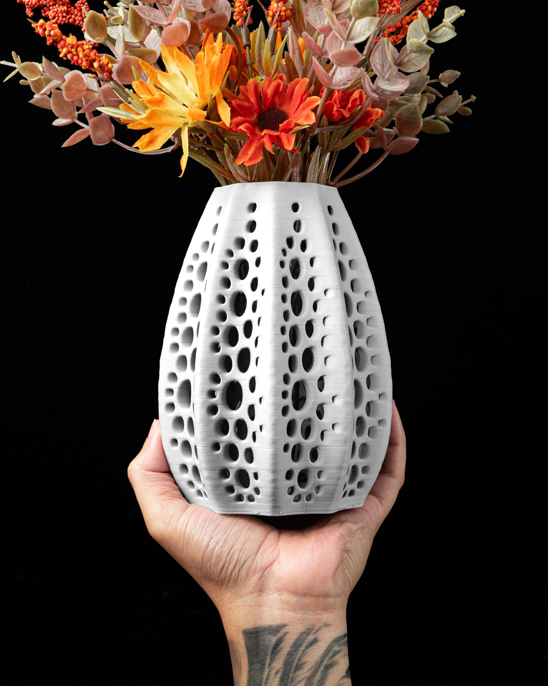 Seashell Flower Vase — weiße 3D-Druck-Vase mit durchbrochenen Voronoi-Kreislöchern, in einer Hand, orange Blüten